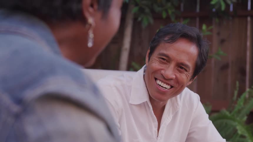 A man smiles at his wife as they sit in chairs outdoors
