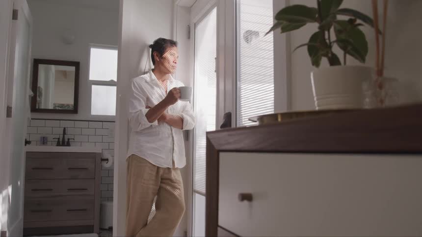 Asian man holding a cup of coffee stands next to the door