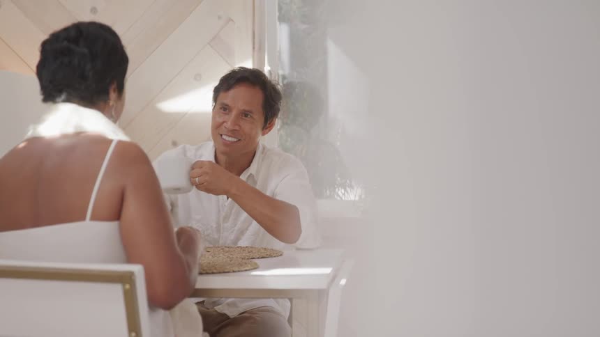 Asian man and woman sitting at the table drink coffee and talk to each other