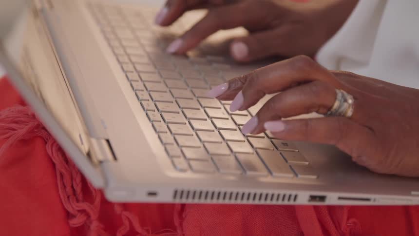 A woman types on a laptop resting on her lap