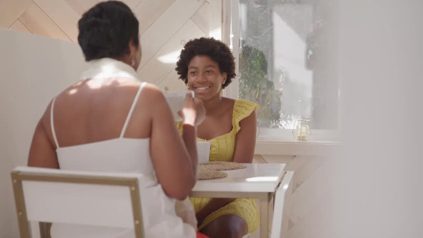 Mother and daughter sitting at a table hanging out drinking coffee