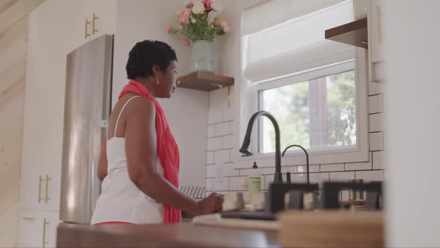 Black woman standing in front of the kitchen sink looks out of the window in the kitchen