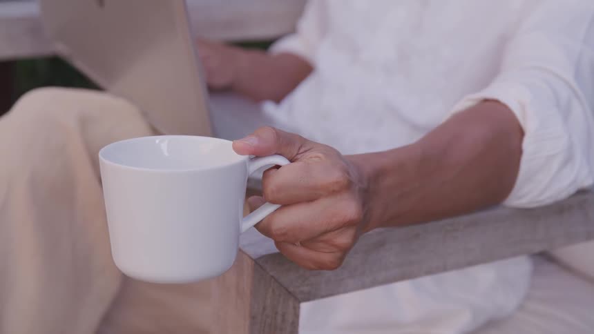 A man uses his laptop while enjoying a drink outdoors