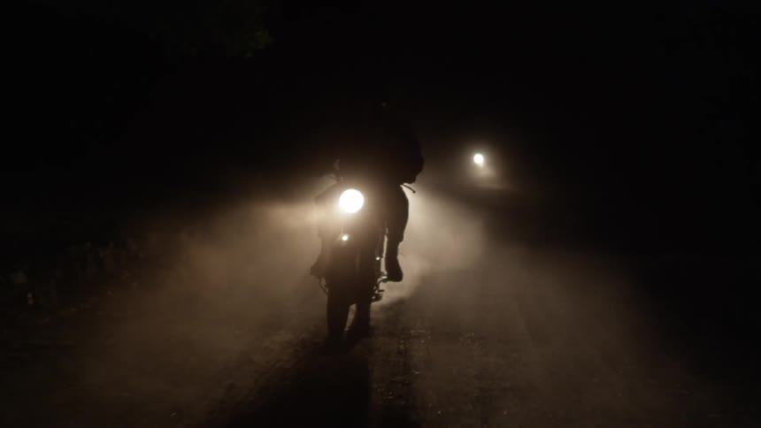 A front view of four motorcycles driving down a dusty path at night