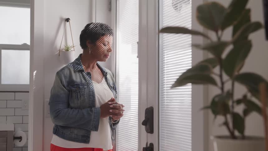 A woman stares through the blinds on a door outside of a bathroom