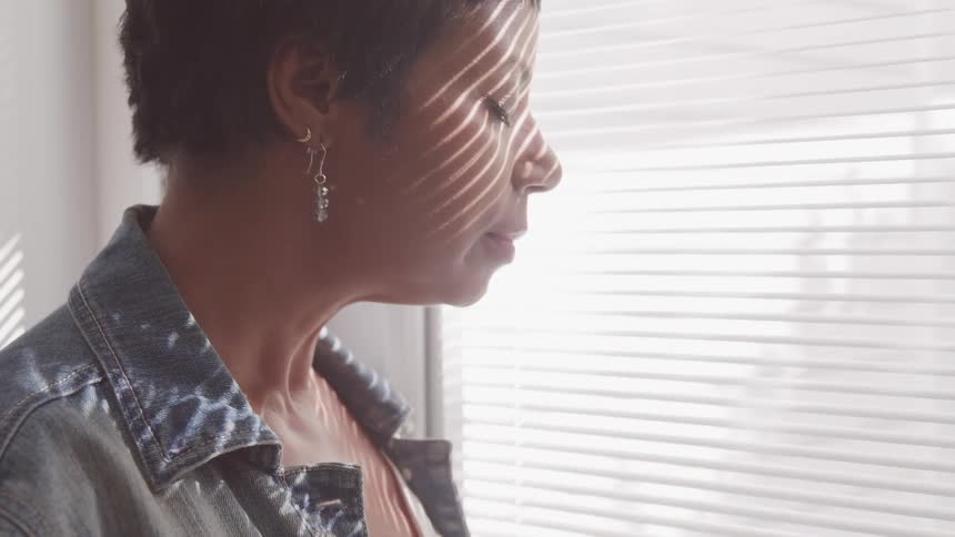 A woman stands before a window with her eyes closed