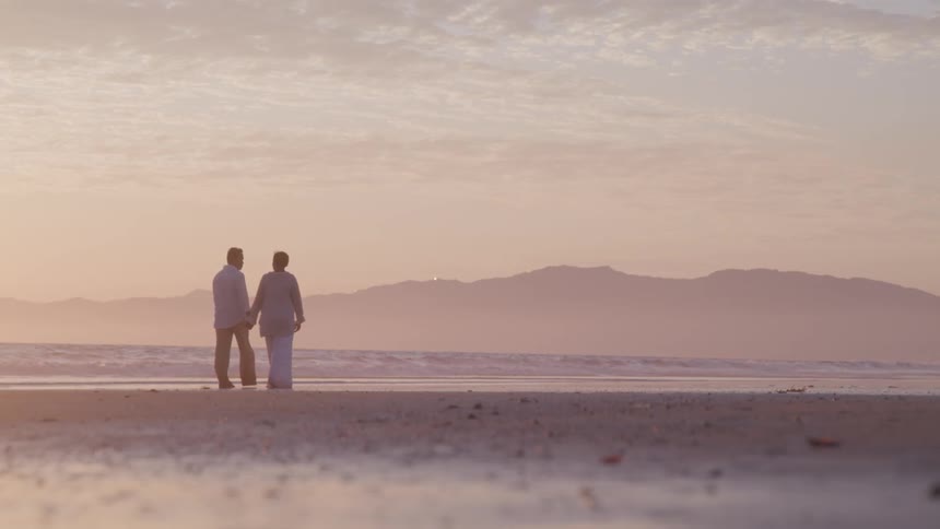 A man and a woman walking on the beach with the sky in the background