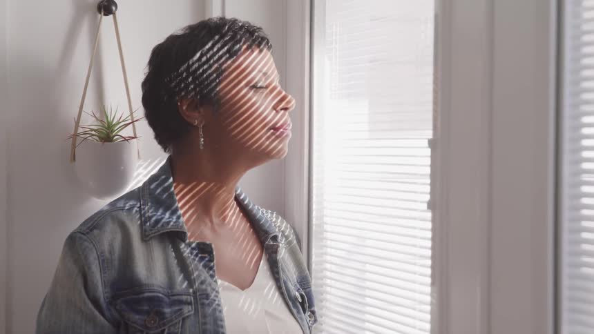 A woman closes her eyes near the window