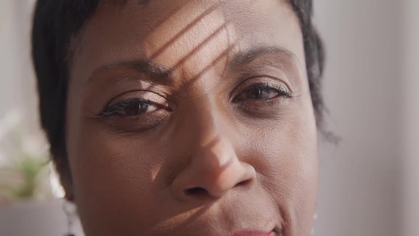The sun shining through window blinds shines on a womans face