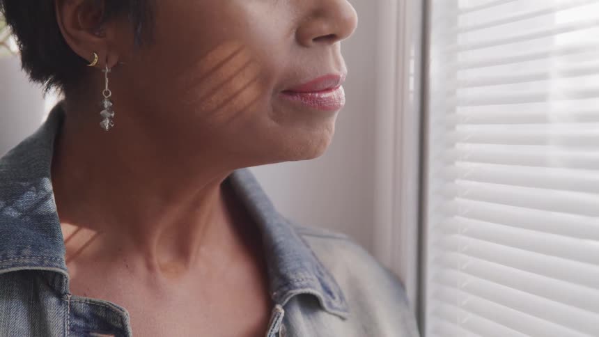 Woman looks outside house through window