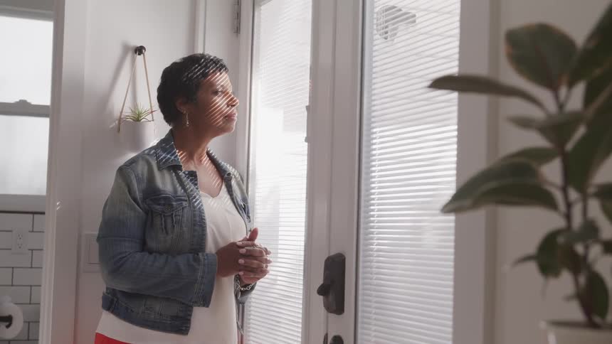 A woman standing inside looking out of a glass door