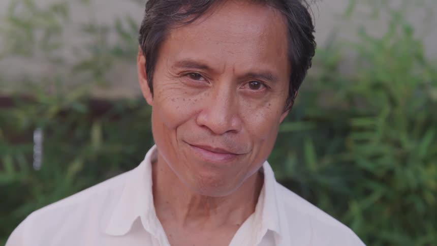 An asian man tilting his head upwards to smile at the camera