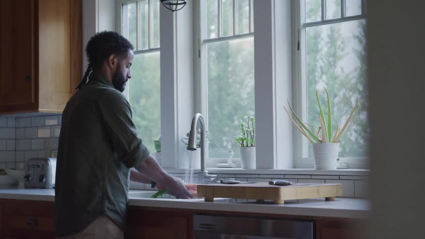 Man washing carrots in kitchen sink near a window