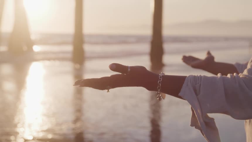 Person with arms wide open standing near to pier on beach at sunset
