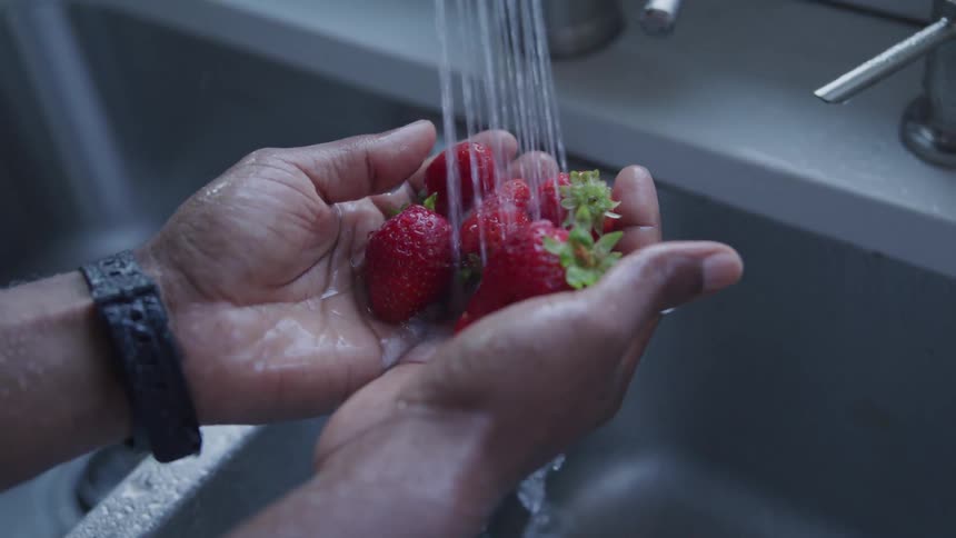 Hands holding strawberries at kitchen sink as flows on them