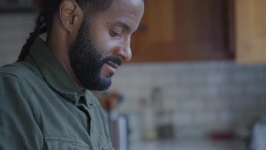 A black man with a ponytail focuses on an activity in a kitchen
