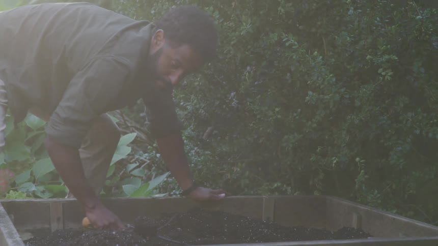 A man is using a hand spade to work the dirt in a garden
