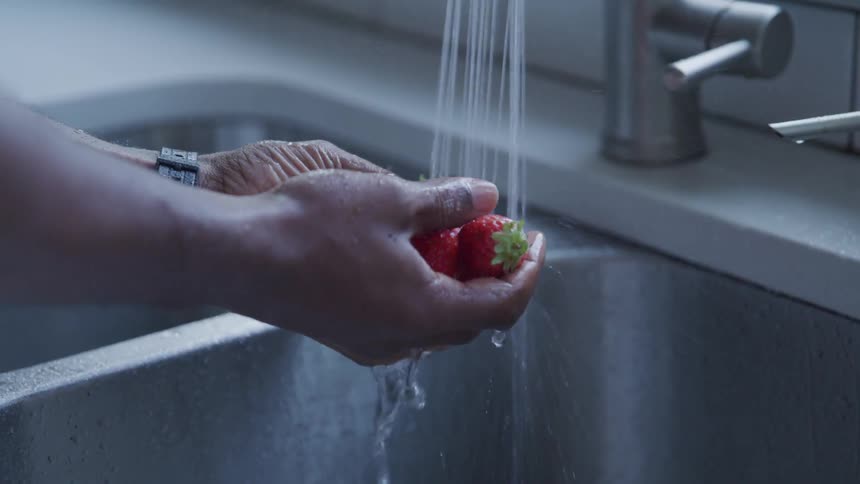 A person rinses off strawberries in a sink