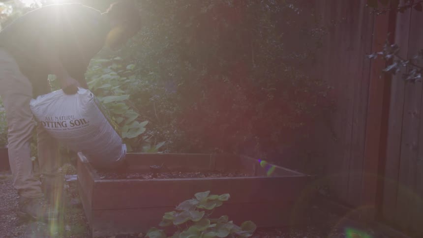 A man dumps potting soil into a raised bed garden
