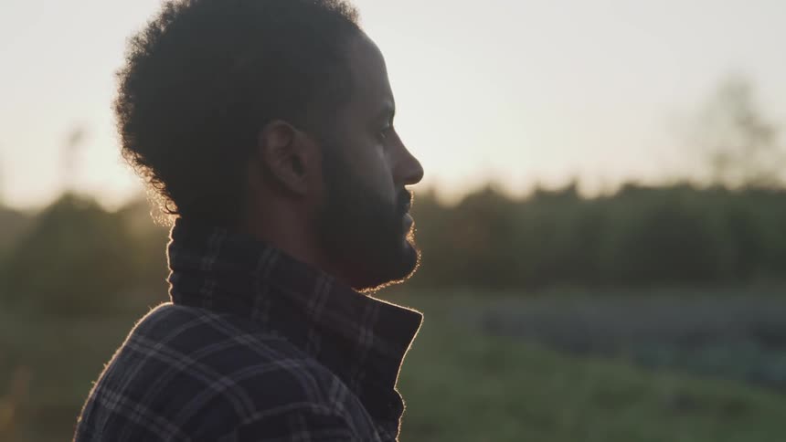 Man stands outdoors looking at field during sunrise