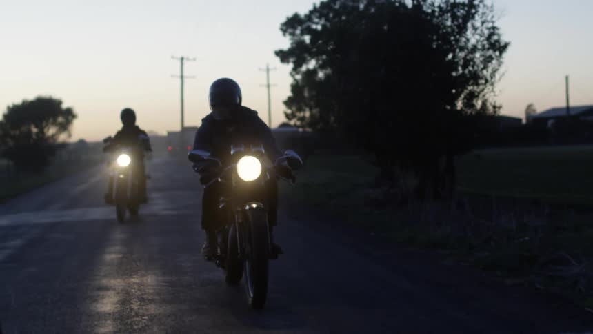 Two men ride motorcycles on a wet road at night