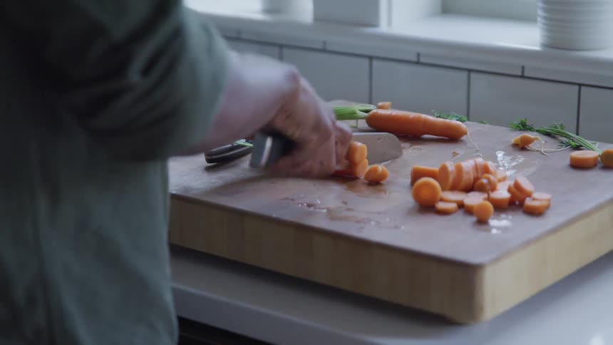 A person uses a knife to chop carrots on a cutting board