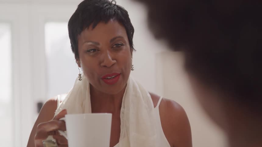 Short hair black woman sitting at the table drinks coffee and talks to her friend in a room