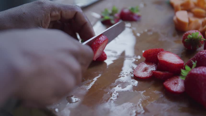 A person slicing strawberries on a wooden cutting board