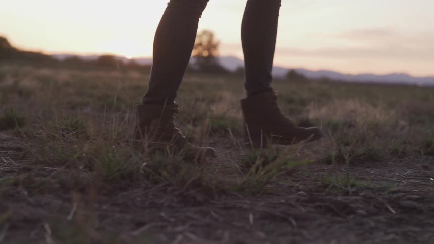 A woman walks through a field at dusk