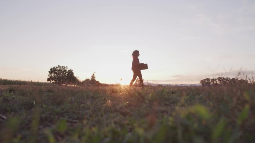 A woman walks across a yard carrying a box