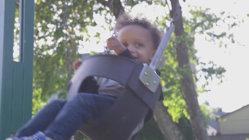 Happy baby swinging in a bucket swing outdoors