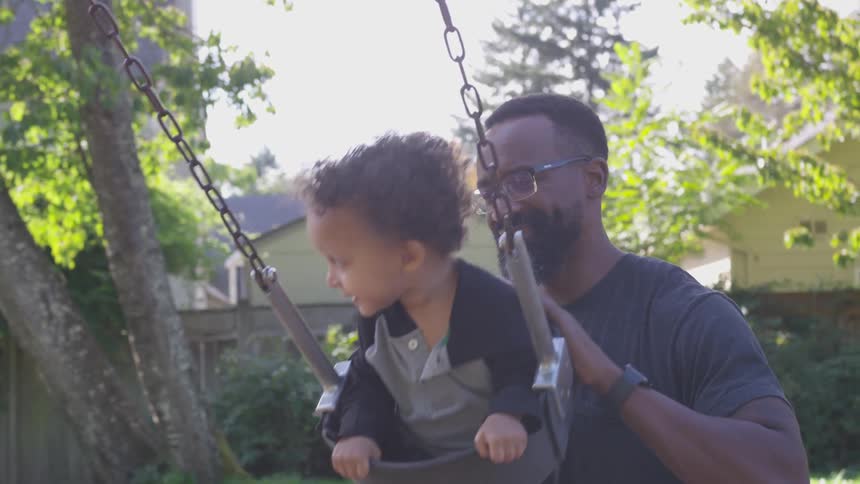 A man pushes his son on a swing in their backyard