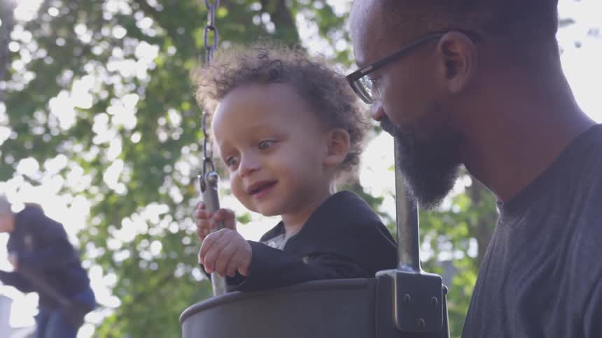 A man plays with a toddler in a swing
