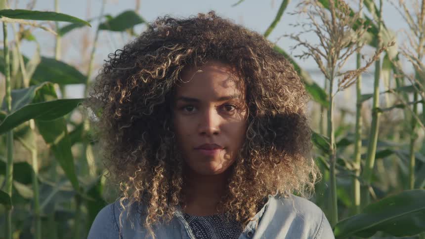 A woman stands in a corn field staring into the camera