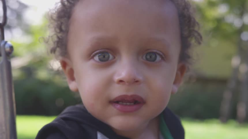 A toddler stares straight forward outside on a summer day