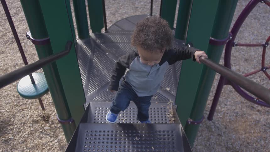 A toddler boy climbs up the stairs of a metal play structure