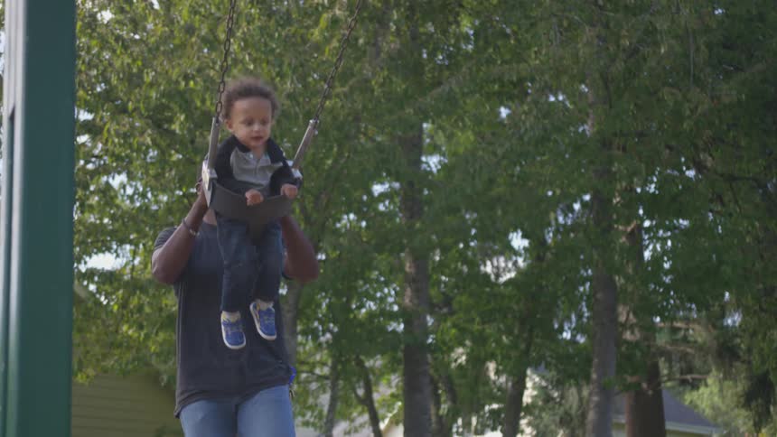 A man pushes a toddler on a park swing