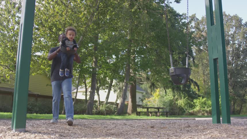 A man pushes a child in the swing