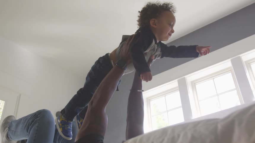 A dad lying on his back holds his toddler son up above him