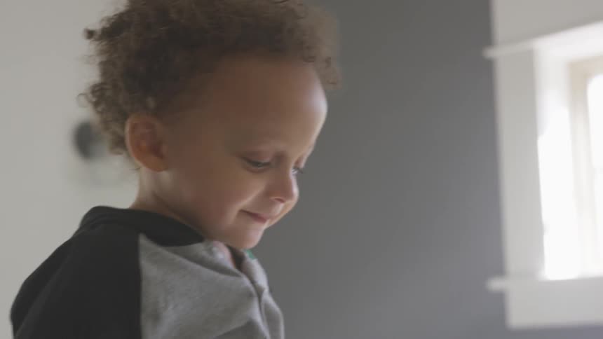 Toddler boy looks down and smiles by jumping in the room during daylight