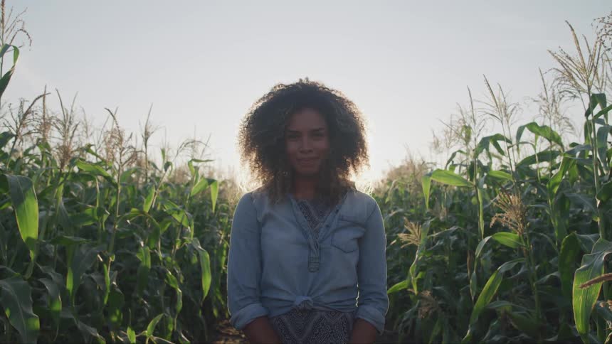 Curly hair brunette woman stands on the forest path and looks at the camera in the field