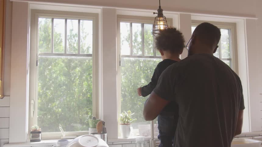 A father holds his son while standing at the kitchen sink