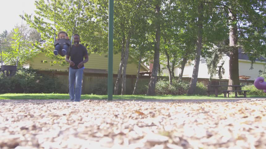 A man pushing a small child in a swing