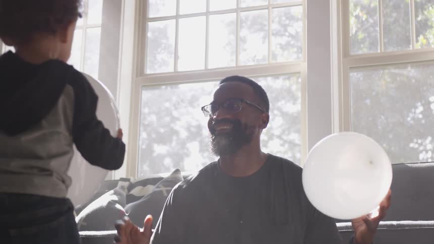 Father and daughter playing with balloons indoors near a window