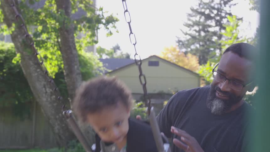 A man pushes a toddler on a swing