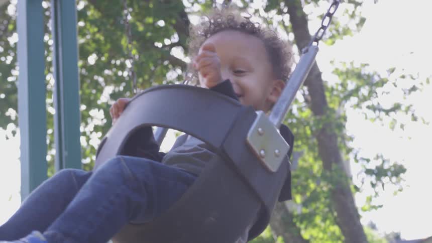 A father is at the park with his child on a swing set