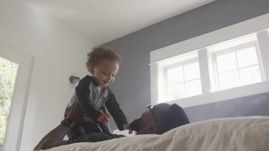 A father and his son play on a bed in a bedroom of a house