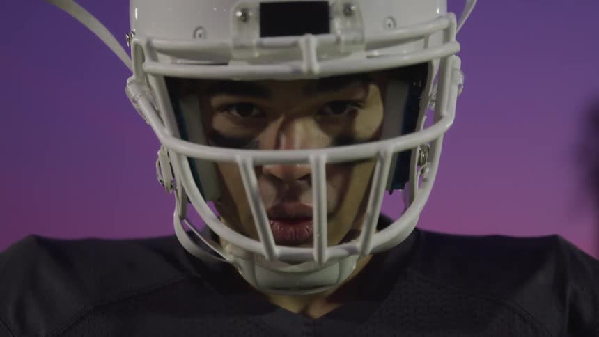 A young black man wearing a football helmet looks determined