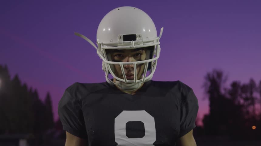Football player standing on football field at sunset looks at camera