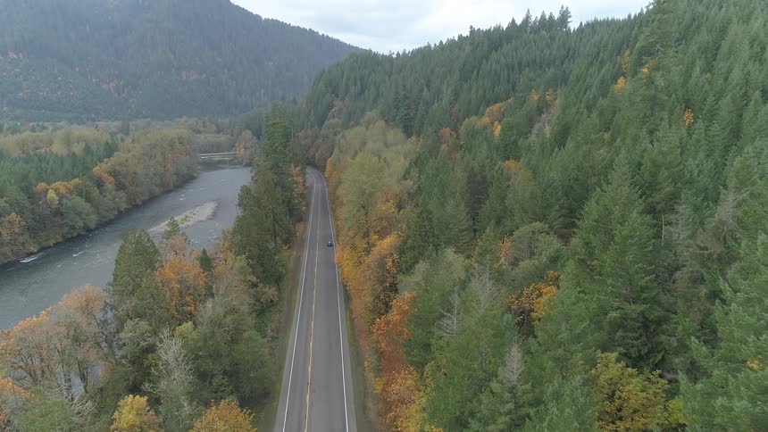 Aerial view of car driving on road going through mountain forest near river